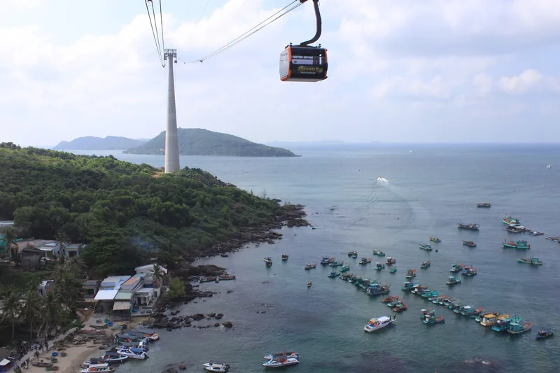 A cable car glides above the coastline near Phu Quoc, with fishing boats dotting the bay below. A cable car glides above the coastline near Phu Quoc, with fishing boats dotting the bay below.