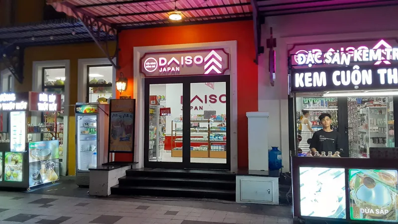 A lit Daiso storefront at night sits between souvenir kiosks on a street in Phu Quoc. A lit Daiso storefront at night sits between souvenir kiosks on a street in Phu Quoc.