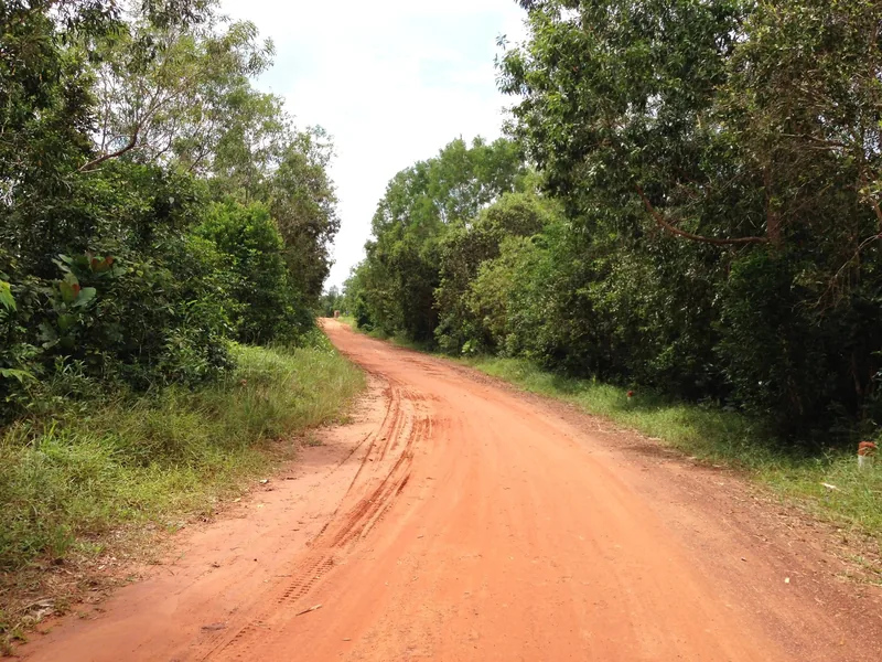 A red dirt road winds through dense green forest on Phu Quoc island, Vietnam.