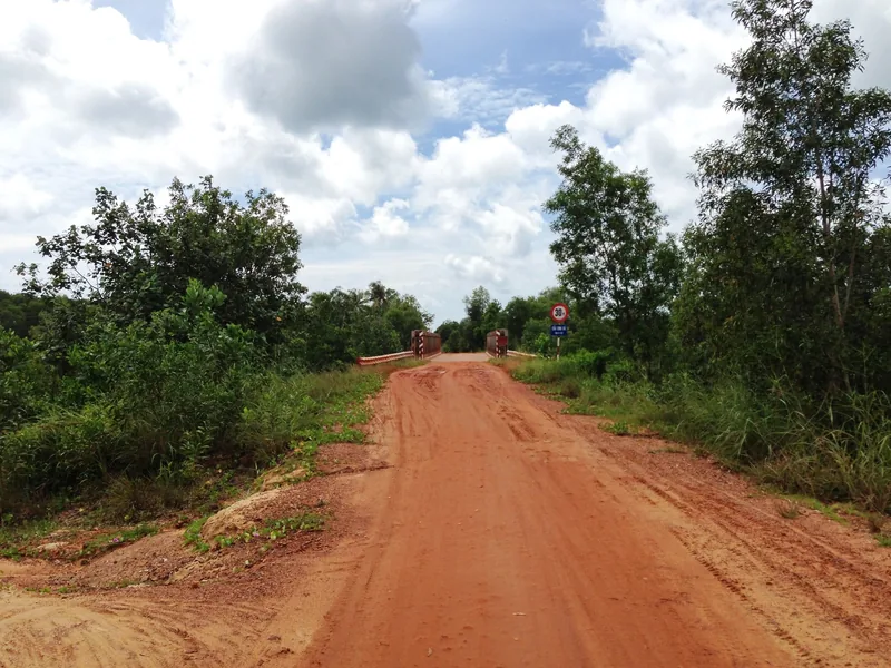 A red dirt road leads through green forest toward a small bridge on Phu Quoc island.