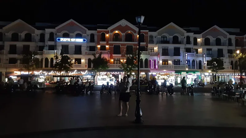 Colorful shophouses glow at night along a plaza in Phu Quoc with people and parked motorbikes.
