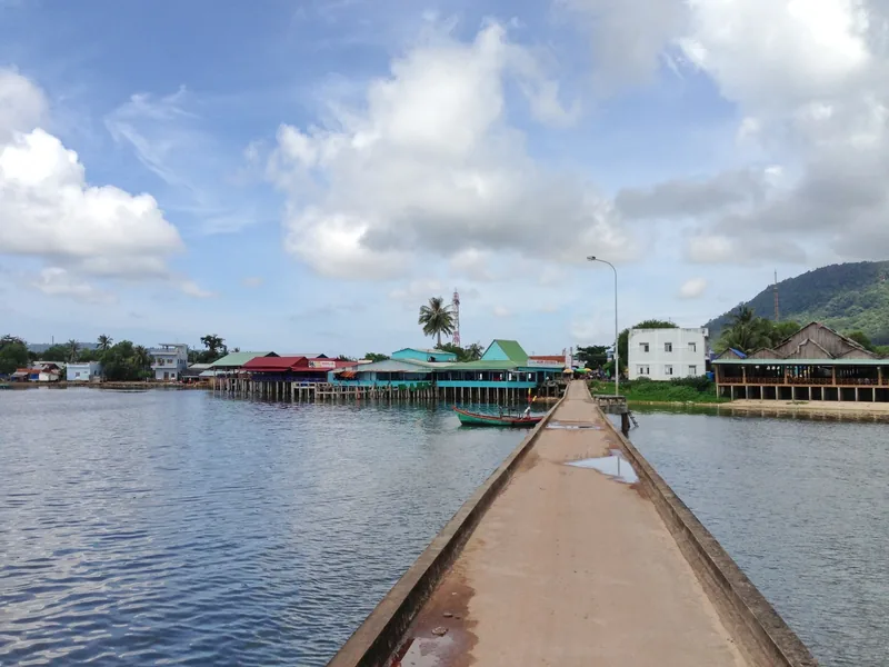 A narrow concrete bridge leads over calm water to the stilt houses of a fishing village in Phu Quoc.