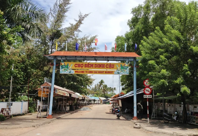 Entrance gate with colorful flags to Dinh Cau Night Market in Duong Dong, Phu Quoc, seen in daytime with empty stalls.