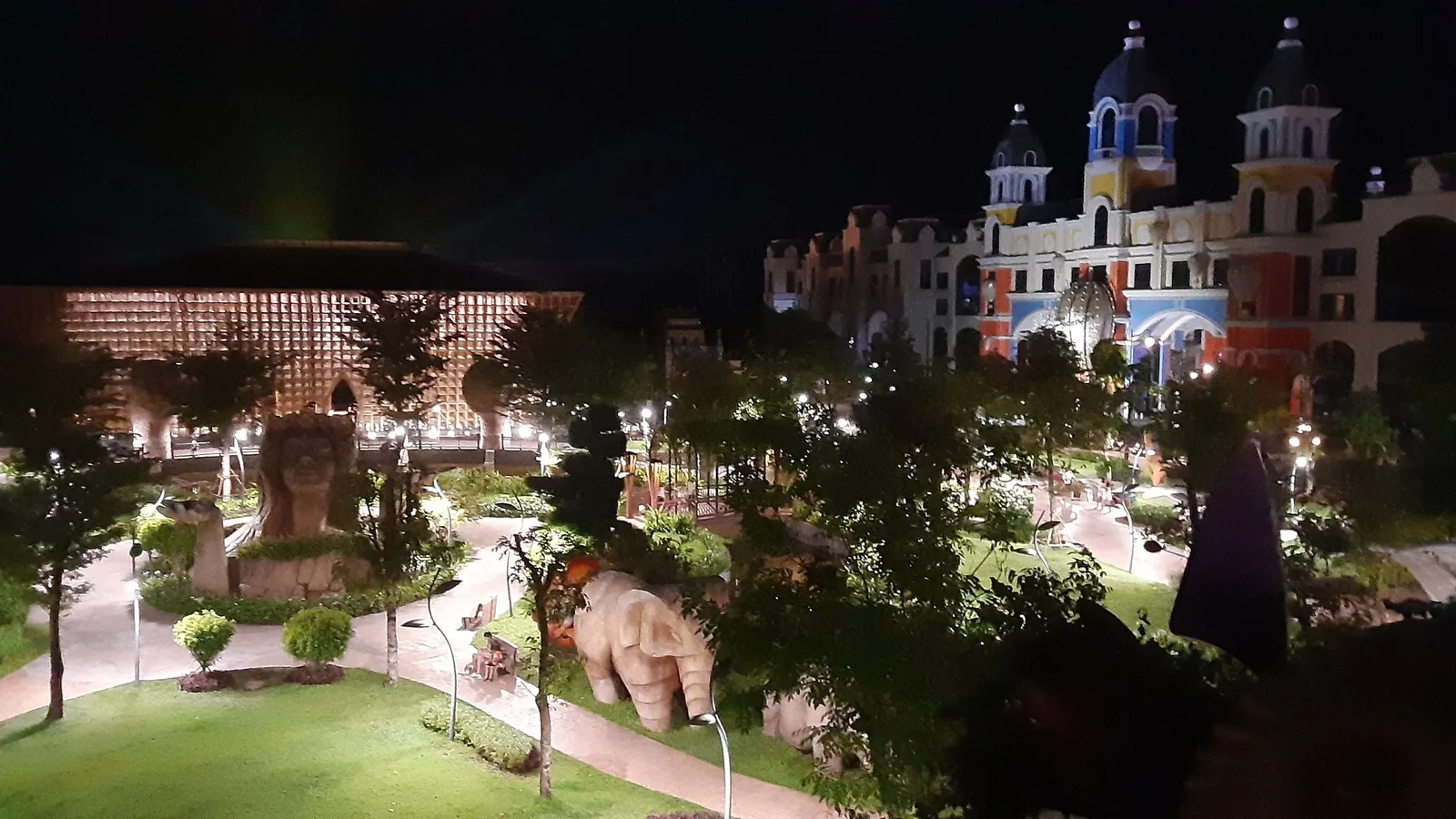Illuminated colonial-style buildings and giant statues glow at night in Grand World Phu Quoc's landscaped park.