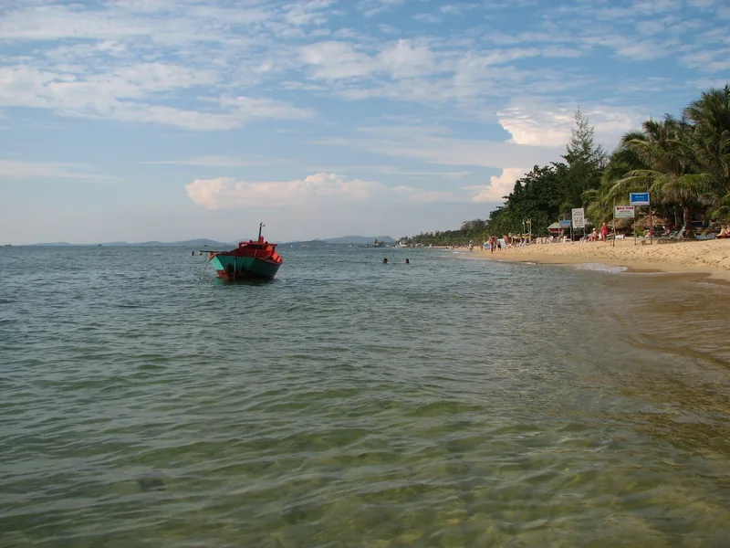 A fishing boat floats near a palm-lined beach with swimmers at Phu Quoc.
