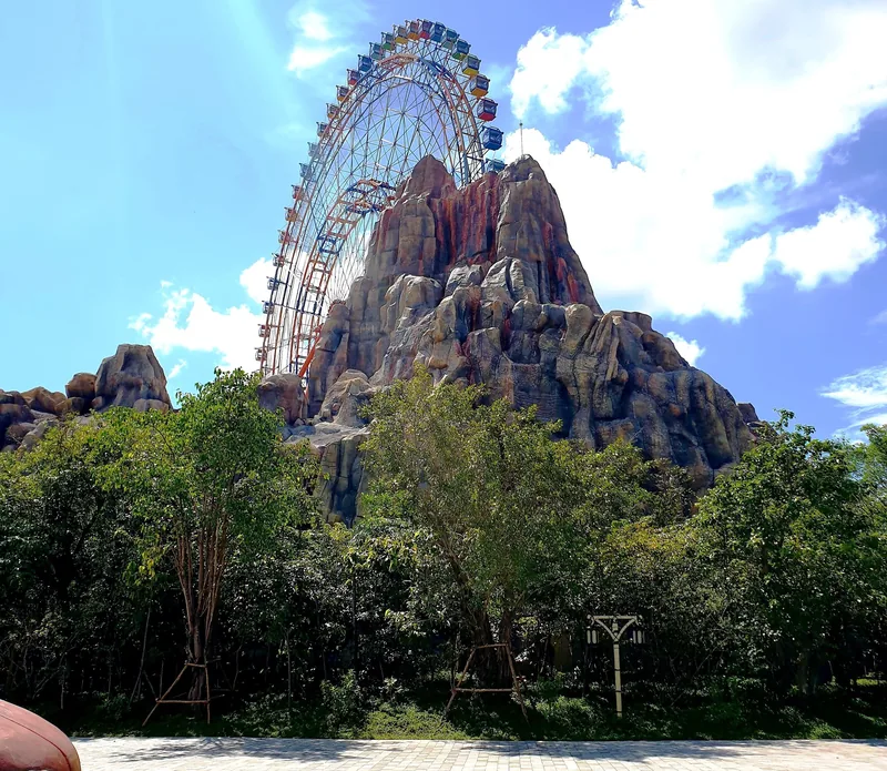 A giant Ferris wheel rises behind an artificial rocky mountain at a theme park in Phu Quoc.