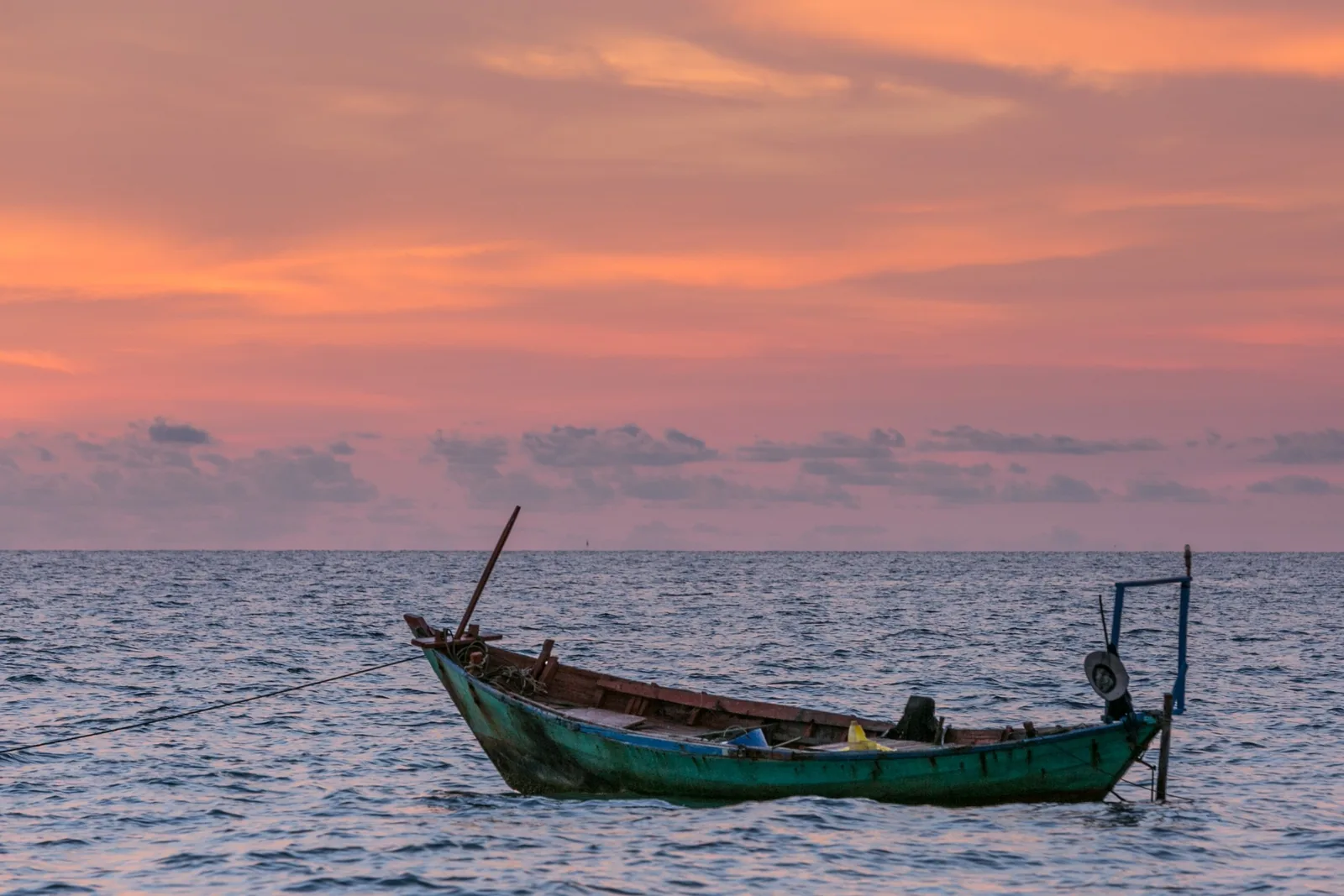 A wooden fishing boat floats calmly on the sea under a pink sunset sky in Phu Quoc.