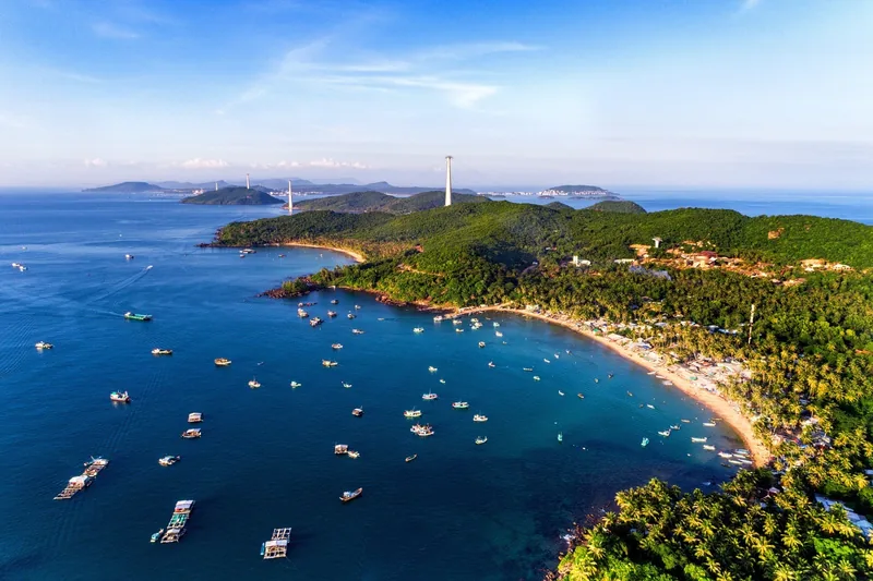 Aerial view of Phu Quoc Island's coastline with fishing boats dotting a curved bay and lush green hills