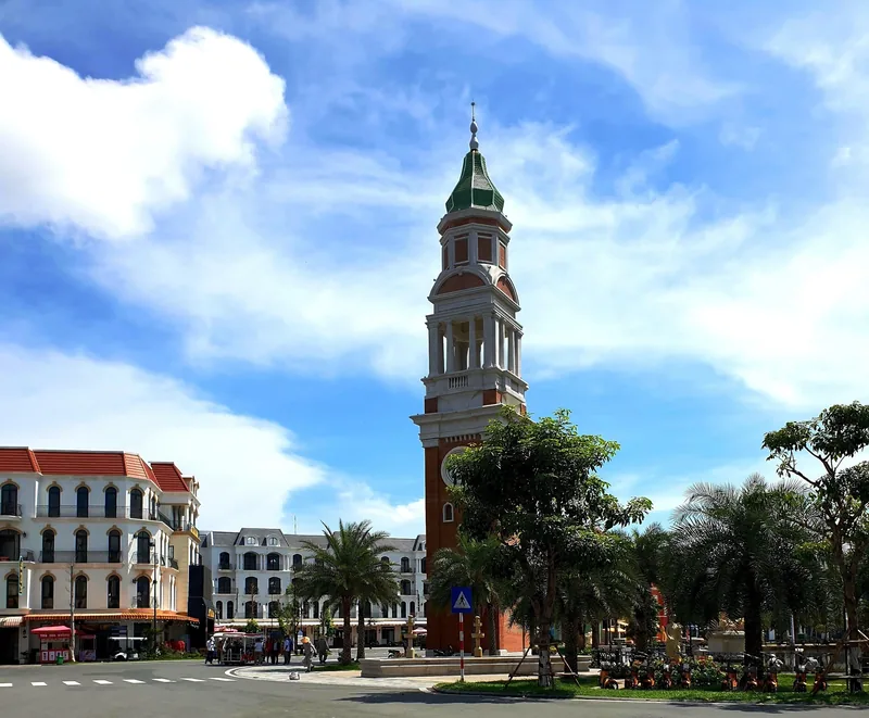 A tall European-style clock tower rises above palm trees and colonial buildings in Phu Quoc.