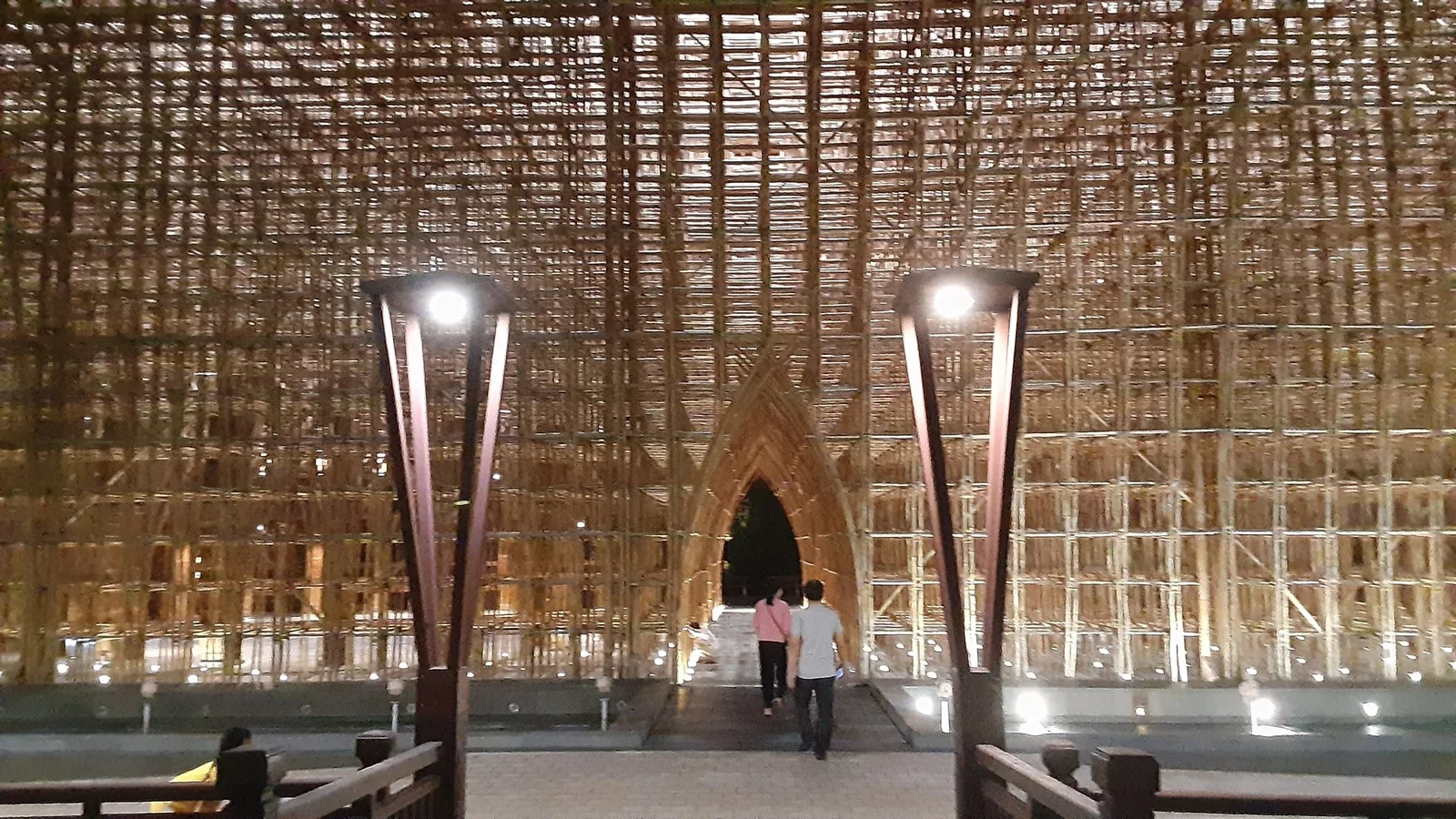 Visitors walk beneath the towering woven bamboo lattice ceiling of a structure at Grand World, Phu Quoc, lit at night.