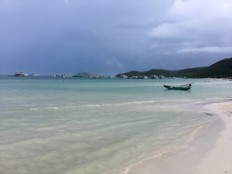A small green boat rests near shore at Bai Sao Beach in Phu Quoc under a stormy sky.