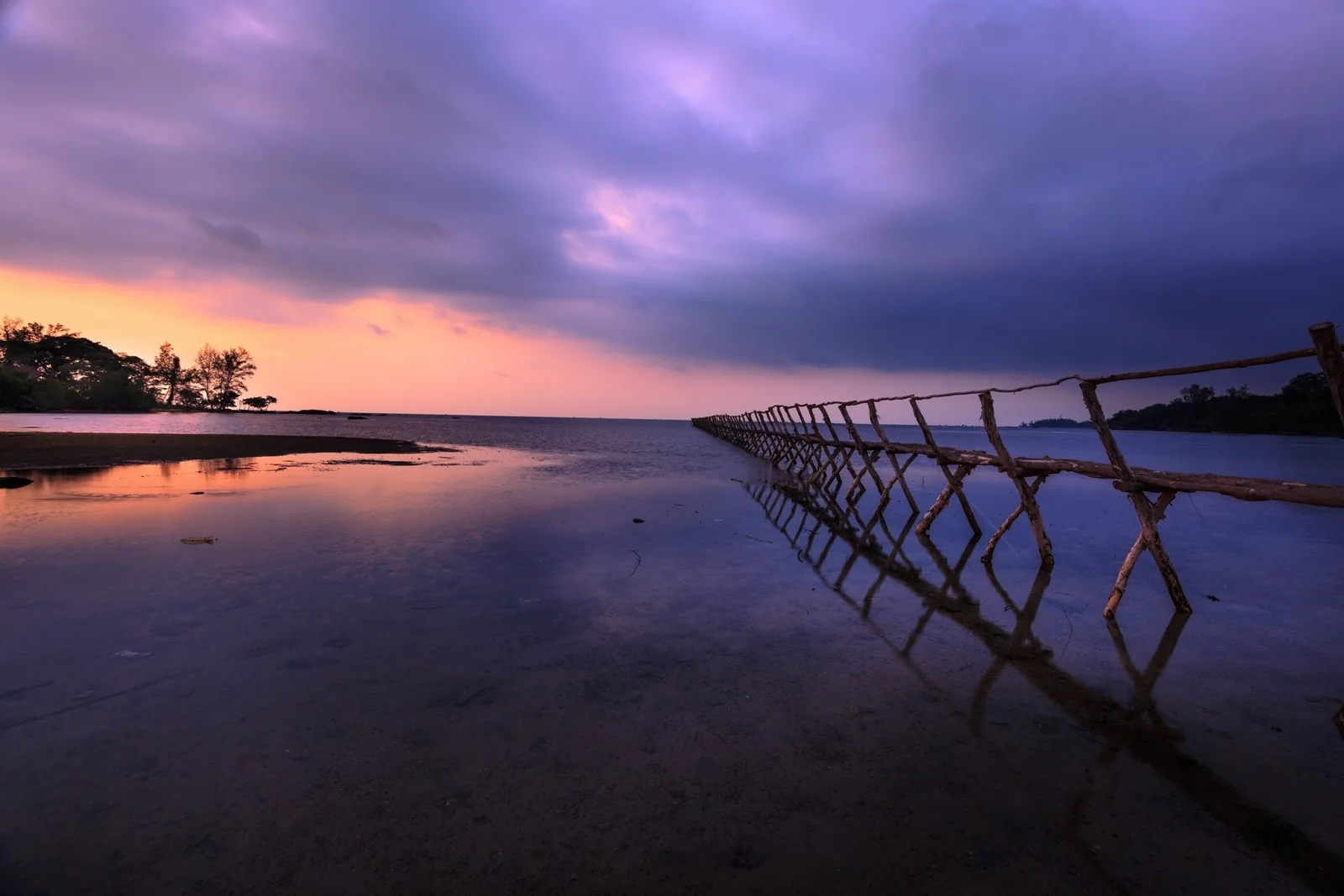 A wooden fishing fence stretches across the shallow tidal flats of Phu Quoc under a dramatic purple sunset sky.