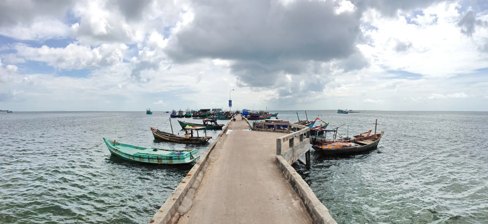 A long concrete pier stretches into the sea with fishing boats moored on both sides near Ham Ninh, Phu Quoc. A long concrete pier stretches into the sea with fishing boats moored on both sides near Ham Ninh, Phu Quoc.