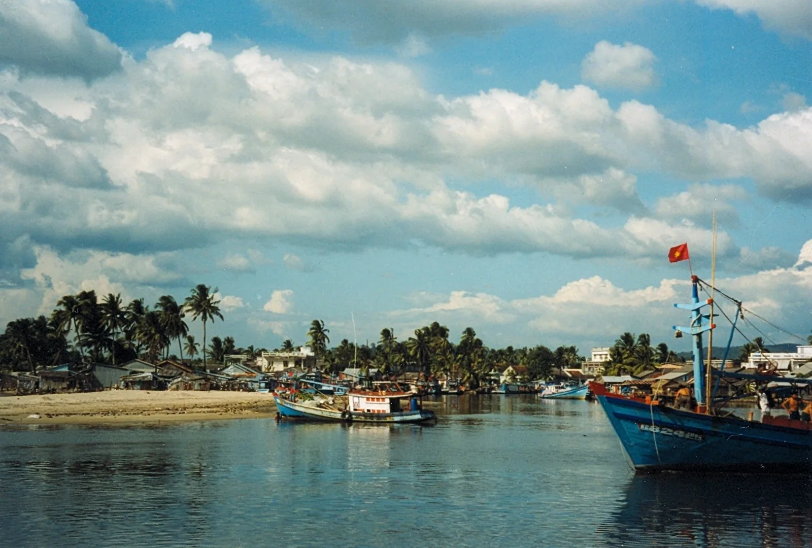 Fishing boats with a Vietnamese flag rest on the calm river at Duong Dong in Phu Quoc under a cloudy sky.