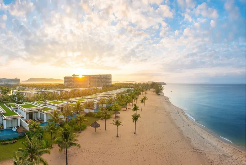 Aerial sunrise view of a beachfront resort with palm trees and villas along a sandy shore in Phu Quoc
