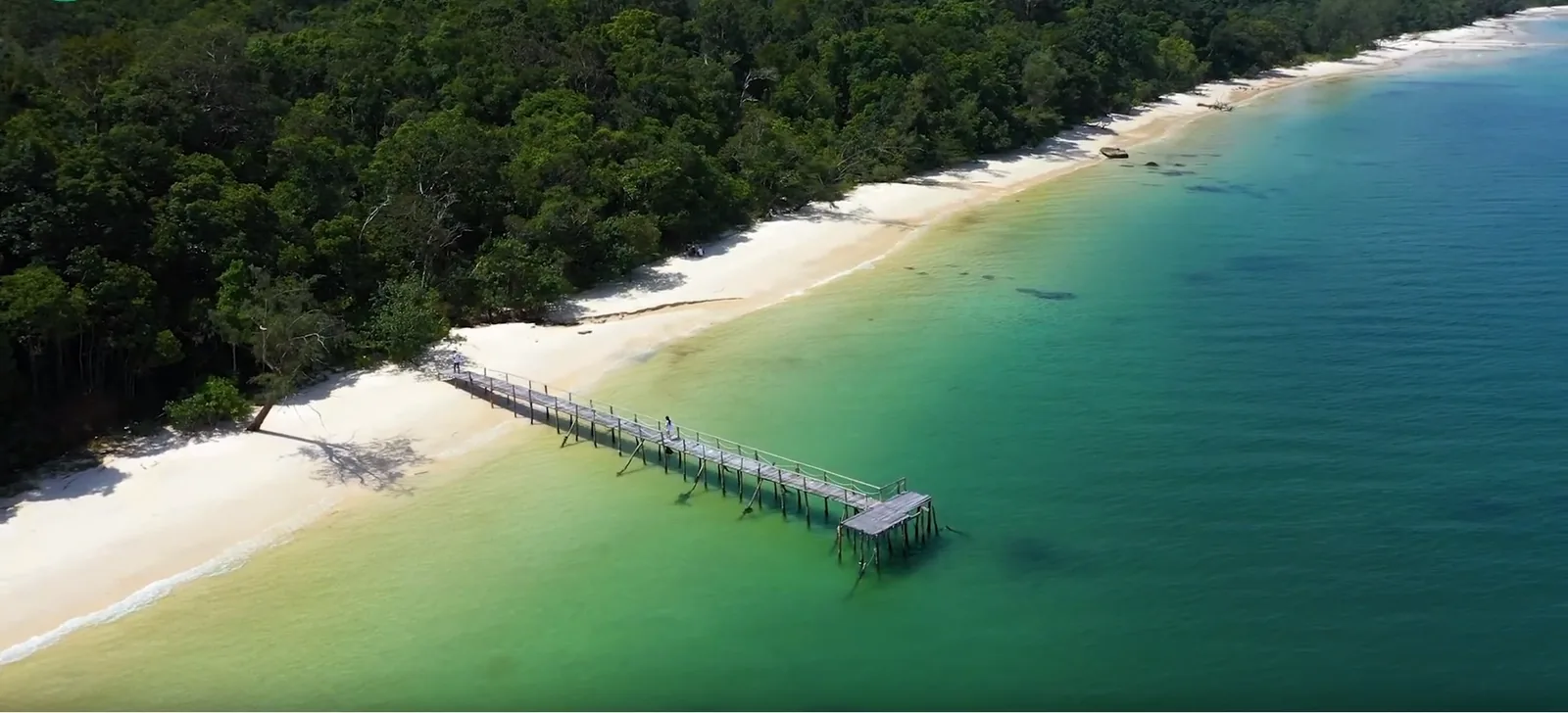 Aerial view of a wooden pier extending into turquoise water along a forested beach near Rach Vem, Phu Quoc.
