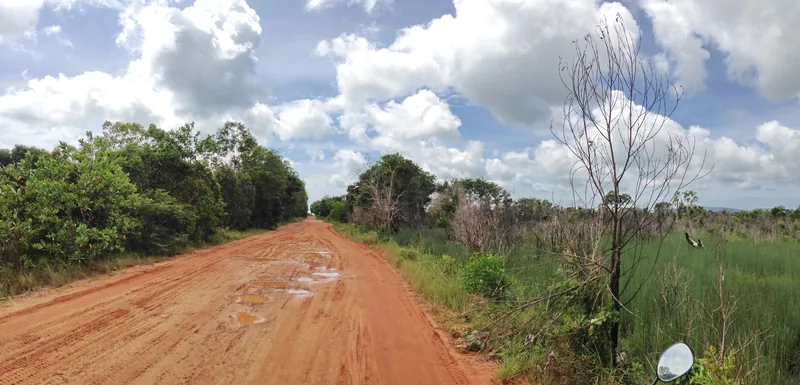 A red dirt road stretches through green forest and grassland under a cloudy sky in Phu Quoc.