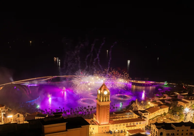 Fireworks and purple lights illuminate a fountain show beside a clock tower at night in Phu Quoc.
