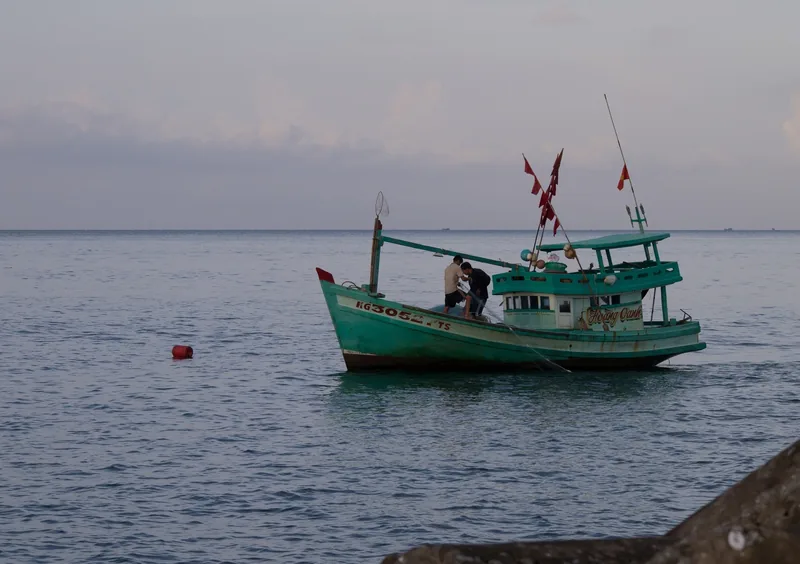 A traditional wooden fishing boat with red flags floats on calm waters off Phu Quoc.