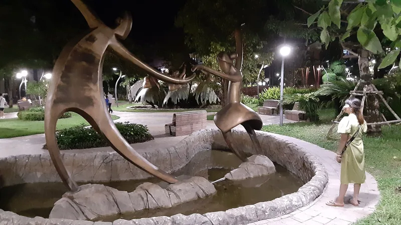 A woman admires abstract bronze sculptures rising from a fountain in a park at night in Phu Quoc.