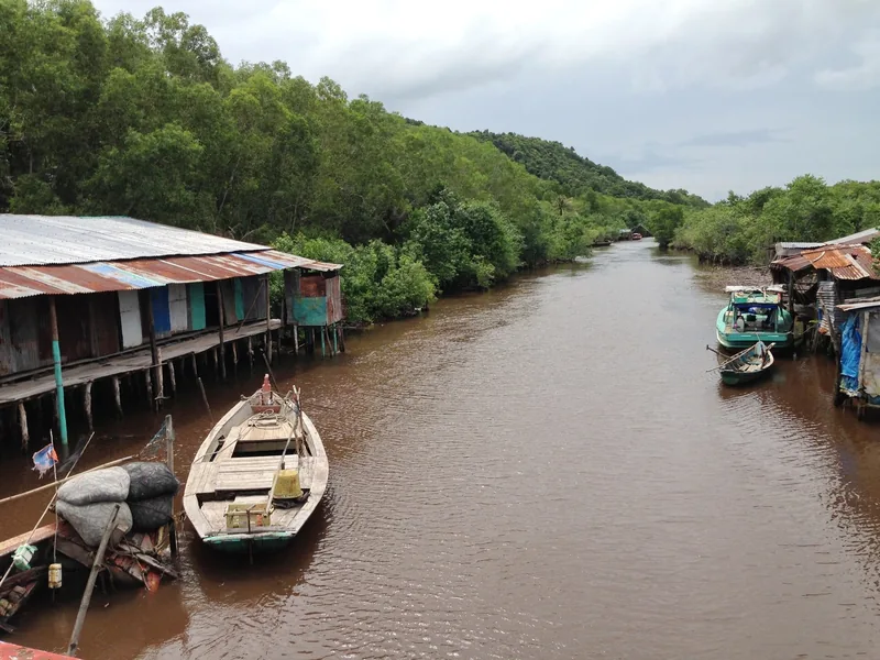Wooden boats moor beside stilt houses along a muddy river lined with mangroves in Phu Quoc.