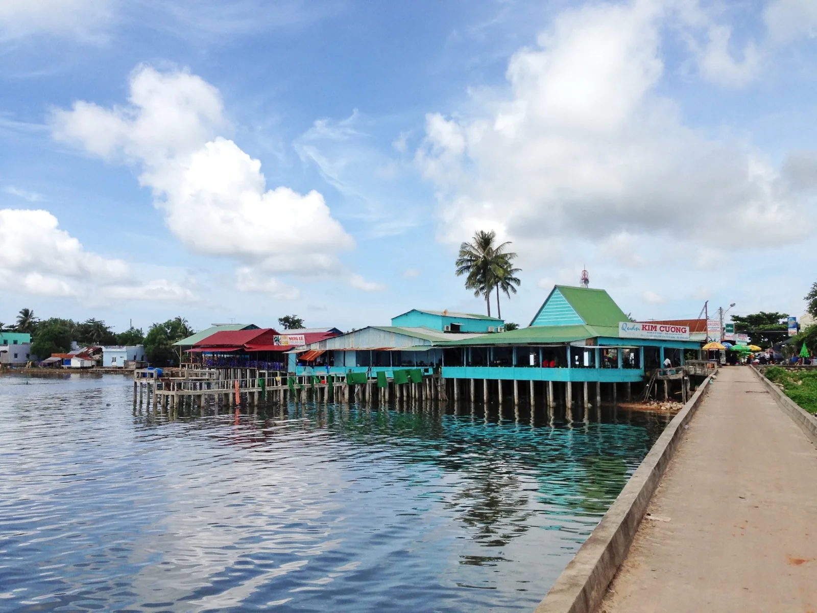 Stilt houses and seafood restaurants line the water at Ham Ninh pier in Phu Quoc under a blue sky.